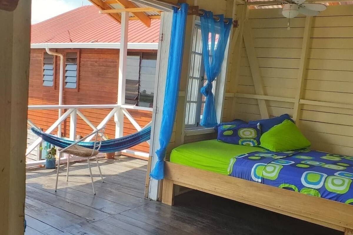 A wooden cabin with a bed, a hammock, and a view of a red-roofed building.