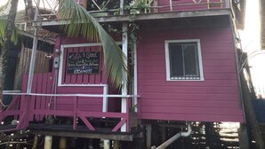 A pink two-story building with a balcony, a signboard, and a palm tree in the foreground. - Life Is Good Casa (Bocas del Toro)