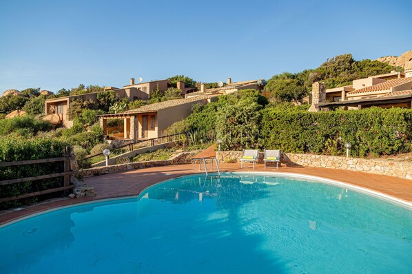 Une piscine dotée d’une terrasse en bois, entourée de murs de pierre et d’une végétation luxuriante.