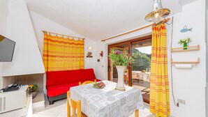 Een kamer met een rode bank, een eettafel met een tafelkleed met patroon, een vaas met bloemen en een geel gordijn.