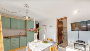 Een keuken met blauwgroene kastjes, een eettafel met een witte tafelkleed en een vaas met bloemen.