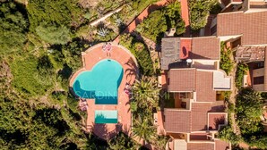 Luchtbeeld van een resort met een groot zwembad, omringd door weelderige begroeiing en terrassen.
