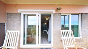 A balcony with two white chairs, a sliding glass door, and a view of the landscape. - Walk to Sandfest, Shared Pools, Boardwalk to the Beach (Port Aransas)