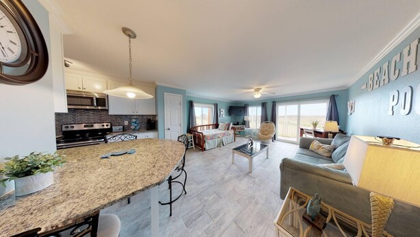 A modern kitchen with granite countertops, a dining area with a bar stool, a living room with a sofa and a coffee table, and a bedroom with a bed and a window. - Walk to Sandfest, Shared Pools, Boardwalk to the Beach (Port Aransas)