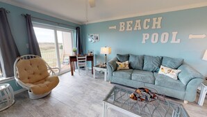 A living room with a blue wall, a sofa, a chair, a coffee table, and a sign that reads "BEACH POOL". - Walk to Sandfest, Shared Pools, Boardwalk to the Beach (Port Aransas)