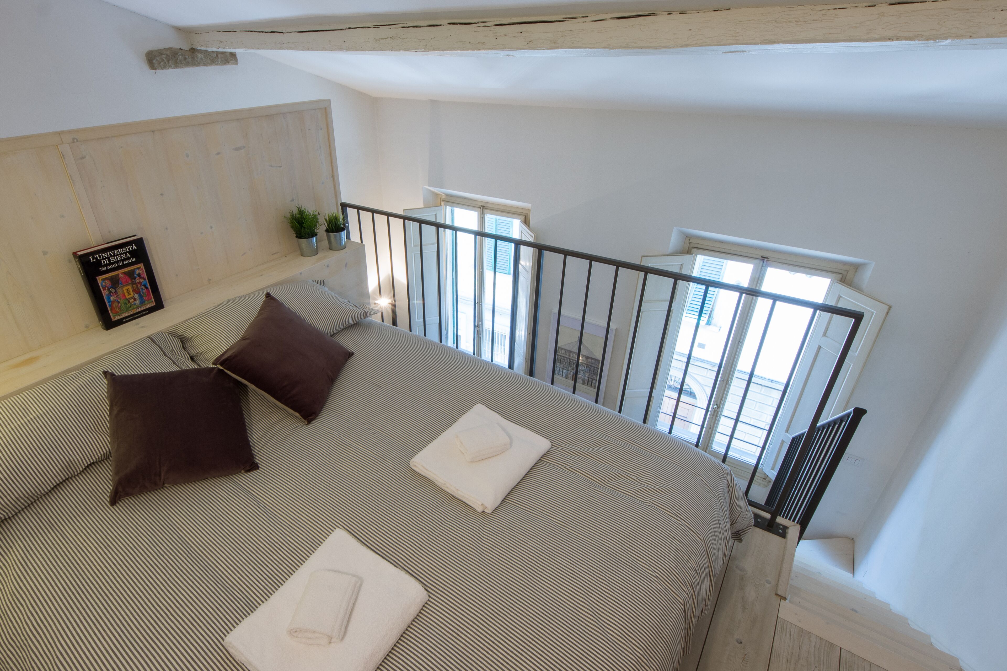 A bedroom with a large bed, a wooden headboard, a small potted plant, and a window with a view of the outside.