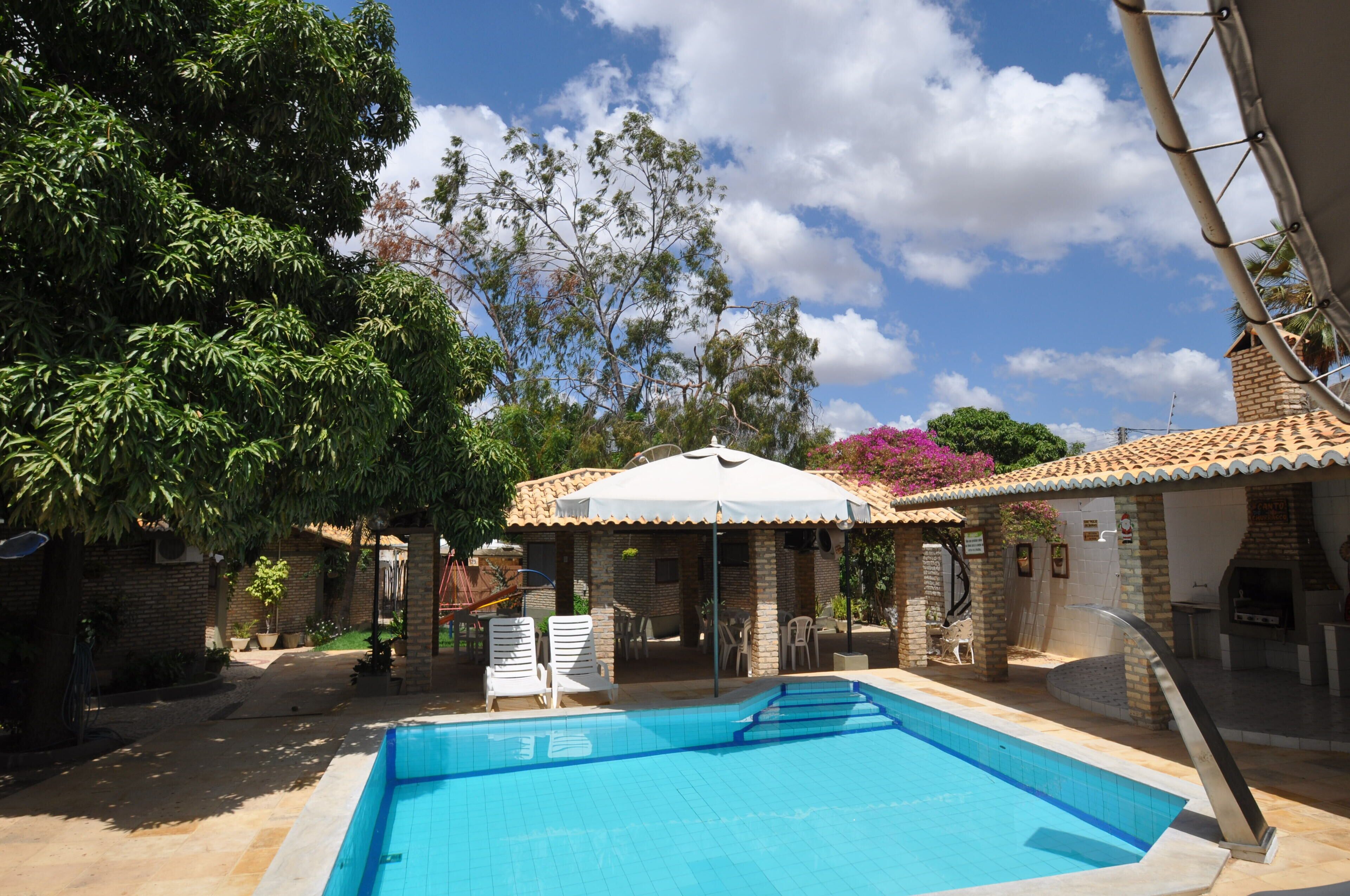 Piscina com deck azulejado, rodeada por um espaço coberto com área de estar ao ar livre.