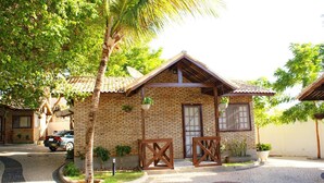 Una casa de dos pisos de ladrillo con techo de tejas, un porche con barandillas de madera y un pequeño jardín con plantas en macetas.