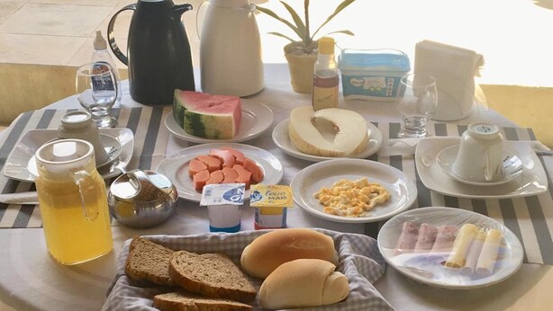 Una mesa de desayuno con diversos alimentos, una cafetera, un hervidor de té y vistas a una piscina.