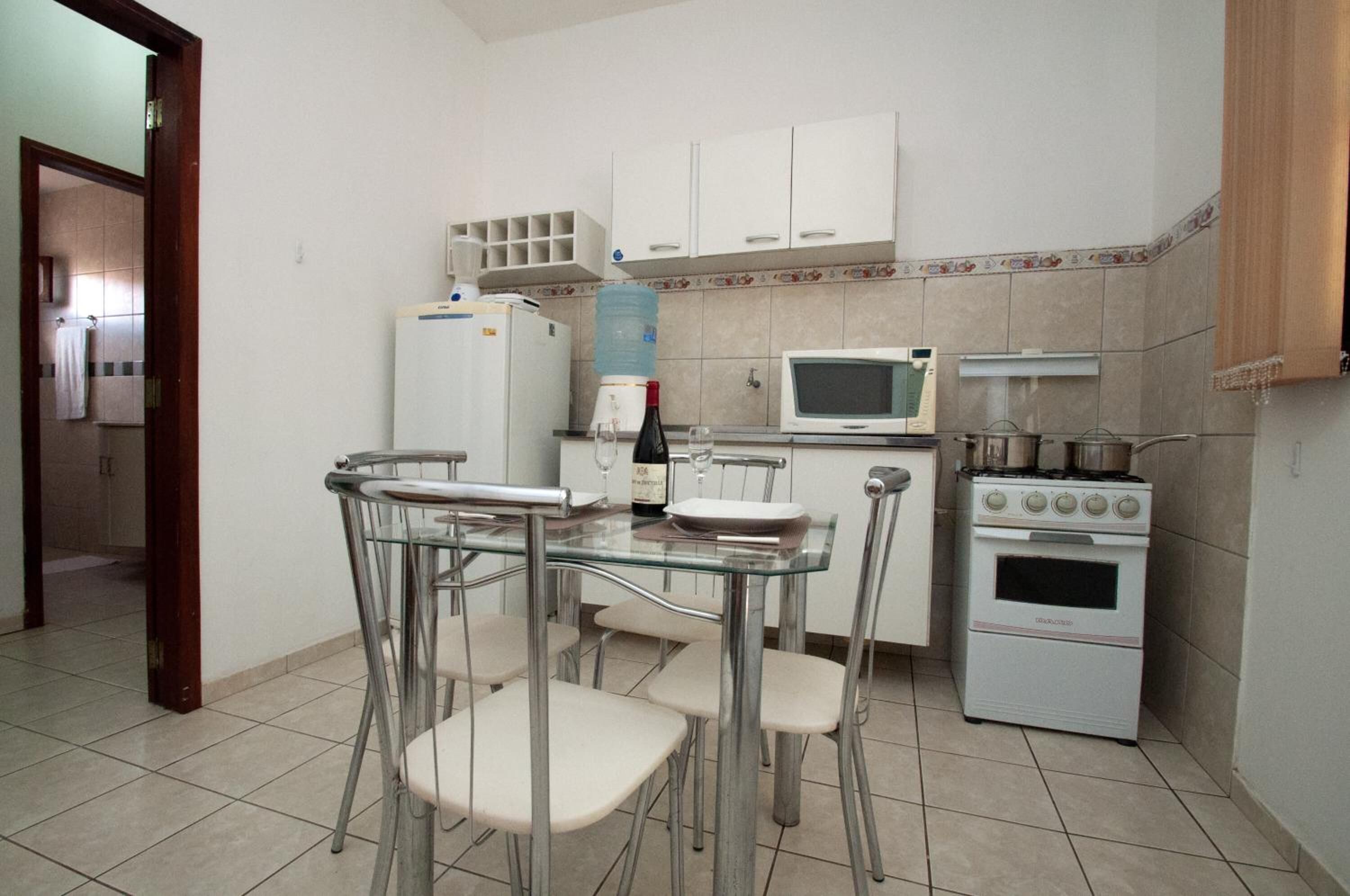 Uma cozinha compacta com geladeira, micro-ondas, fogão e uma mesa de jantar com tampo de vidro e cadeiras.