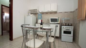Uma cozinha compacta com geladeira, micro-ondas, fogão e uma mesa de jantar com tampo de vidro e cadeiras.