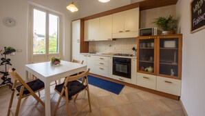 Uma cozinha moderna com armários brancos, uma mesa de jantar com cadeiras, um relógio e uma placa de boas-vindas.