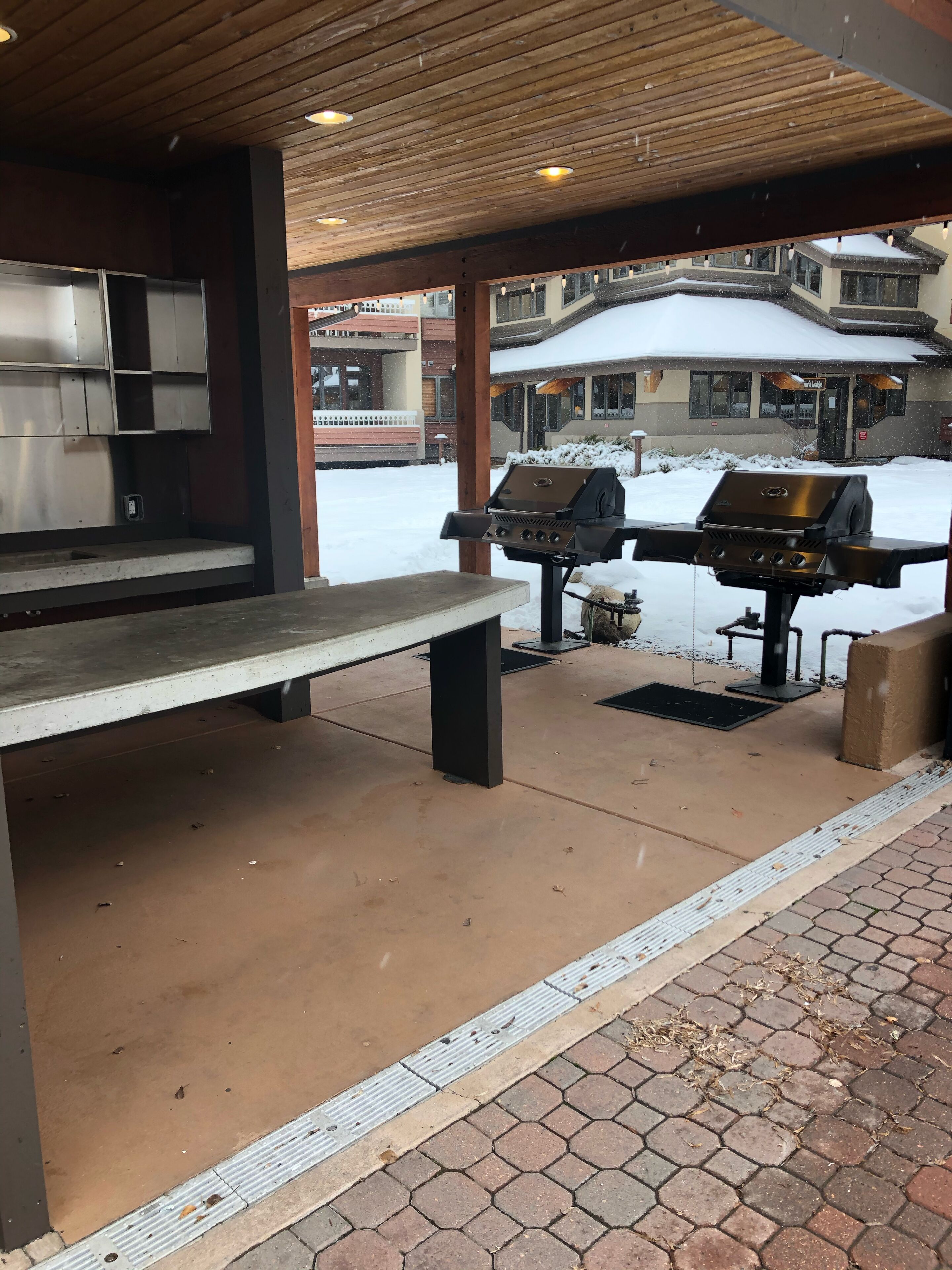 An outdoor patio with a grill, a bench, and a covered area with a wooden ceiling.