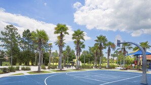 Un terrain de basket entouré de palmiers et une aire de jeux avec un toit rouge.