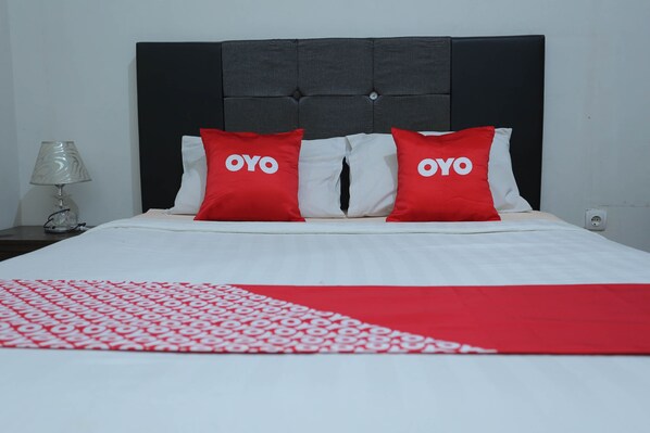 Un lit avec une tête de lit noire, une literie blanche et deux oreillers rouges ornés du texte « OYO ».