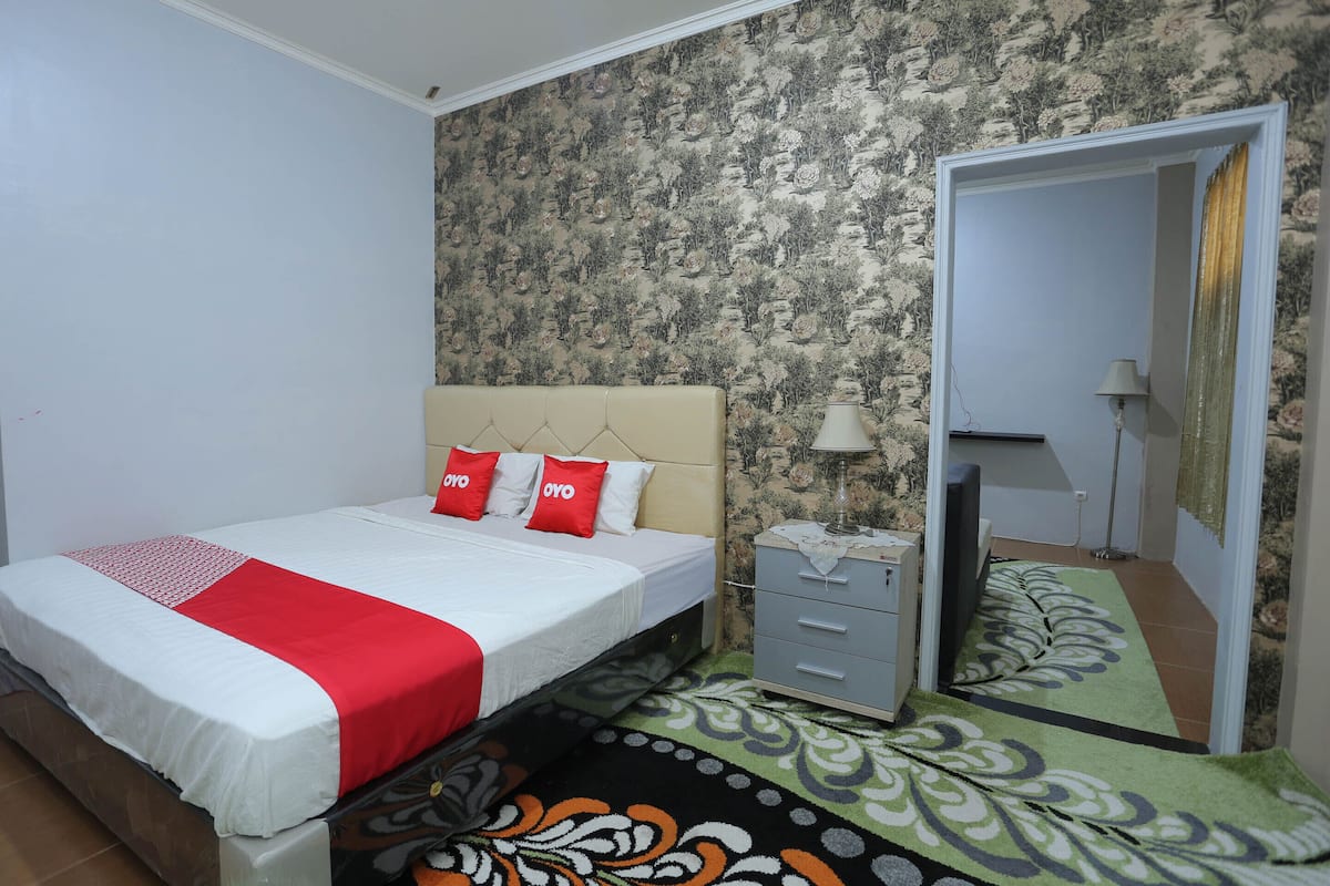 Un dormitorio con cama, cómoda, espejo y alfombra estampada.
