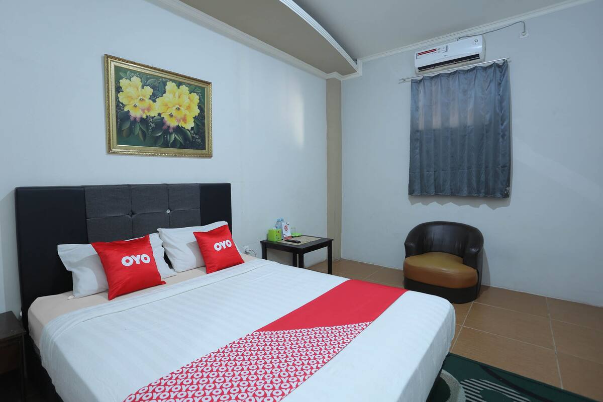Habitación de hotel con cama, mesita de noche, una silla, un cuadro y un equipo de aire acondicionado.