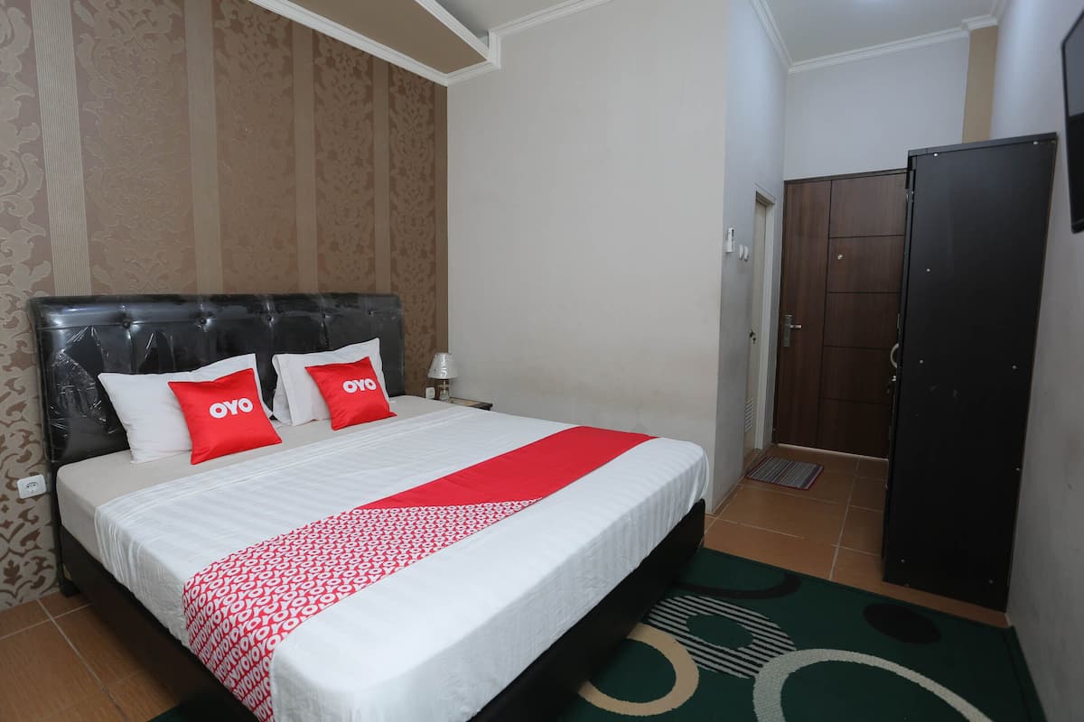 Habitación de hotel con cama, dos almohadas, mesita de noche, lámpara, armario y puerta.