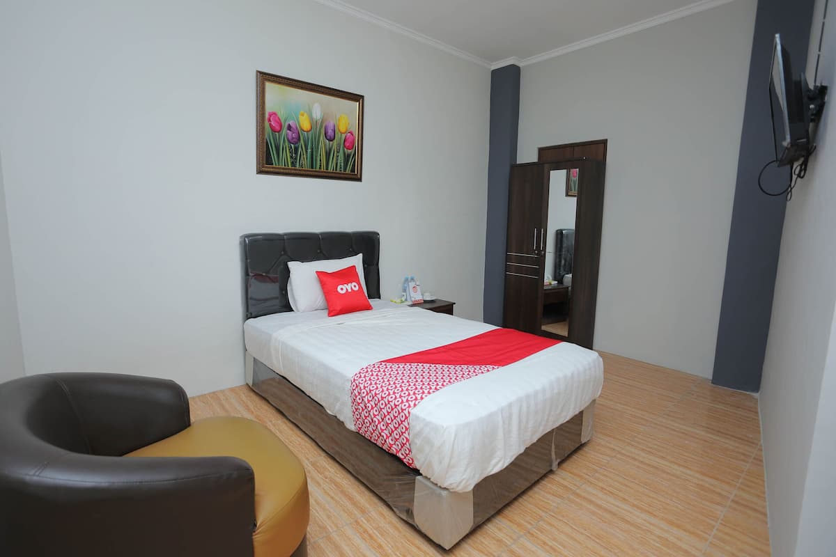 Habitación de hotel con cama, una silla, una mesita de noche, un espejo y un cuadro en la pared.