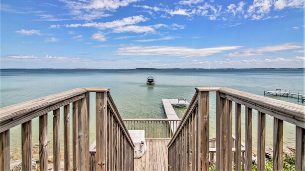 Une terrasse en bois qui mène à une étendue d’eau calme, avec un bateau visible au loin.