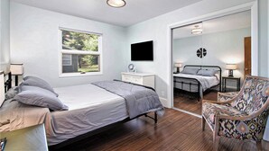 Une chambre à coucher avec un lit, des tables de chevet, une chaise, une télévision, un miroir et une fenêtre.