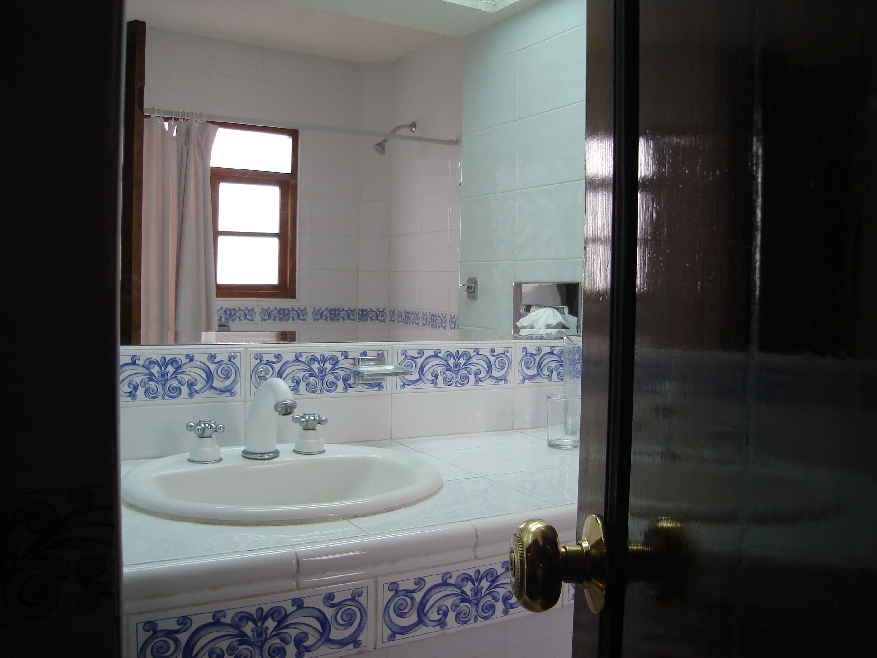 A bathroom with a white sink, blue decorative tiles, a shower, and a window with curtains.