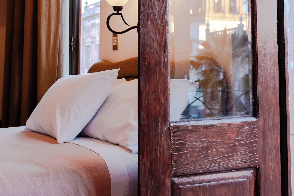 A hotel room with a bed, a window, and a lamp.