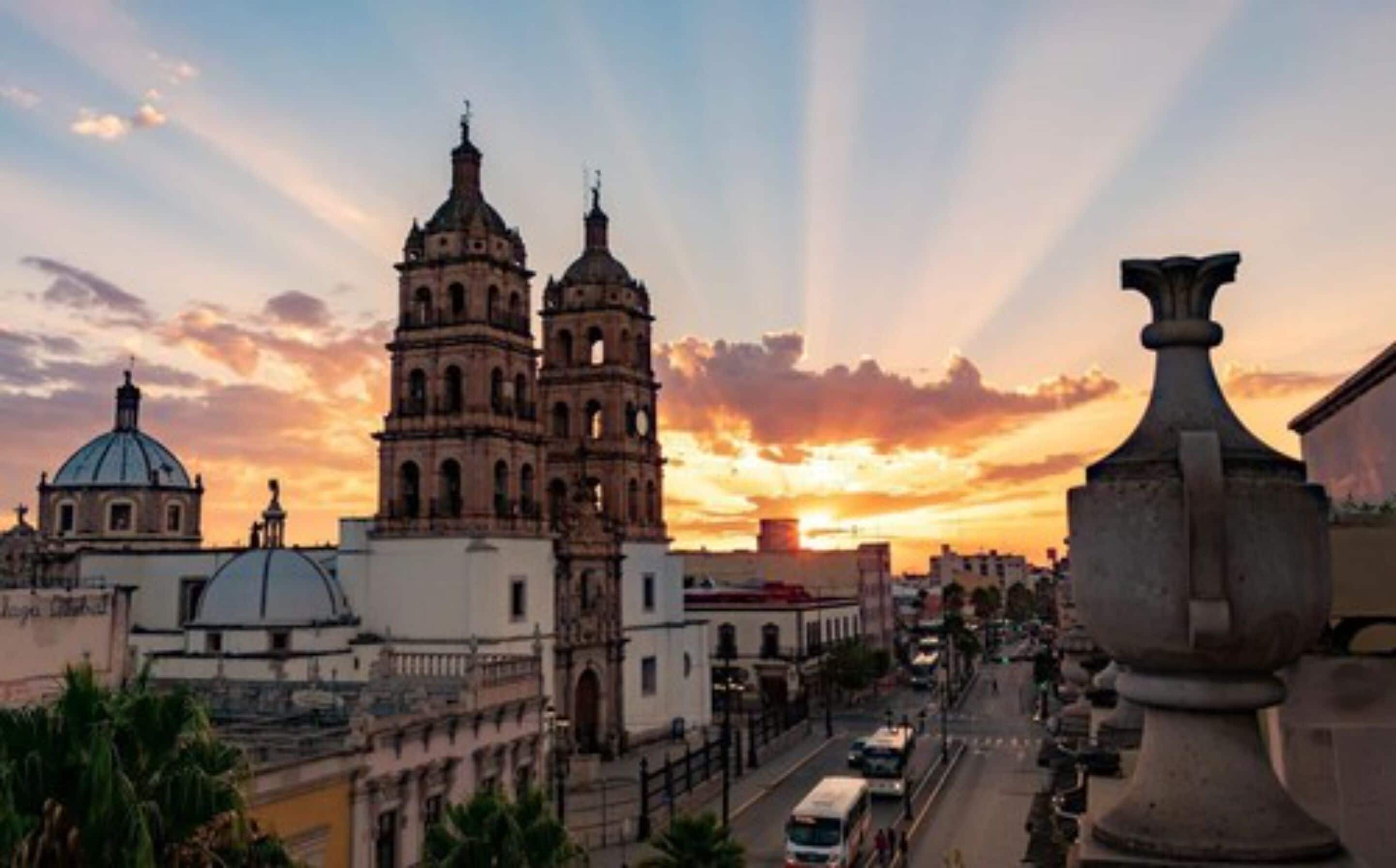 A historic building with two bell towers and a dome, surrounded by urban streets and vehicles.