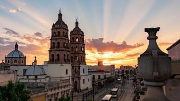 A historic building with two bell towers and a dome, surrounded by urban streets and vehicles.