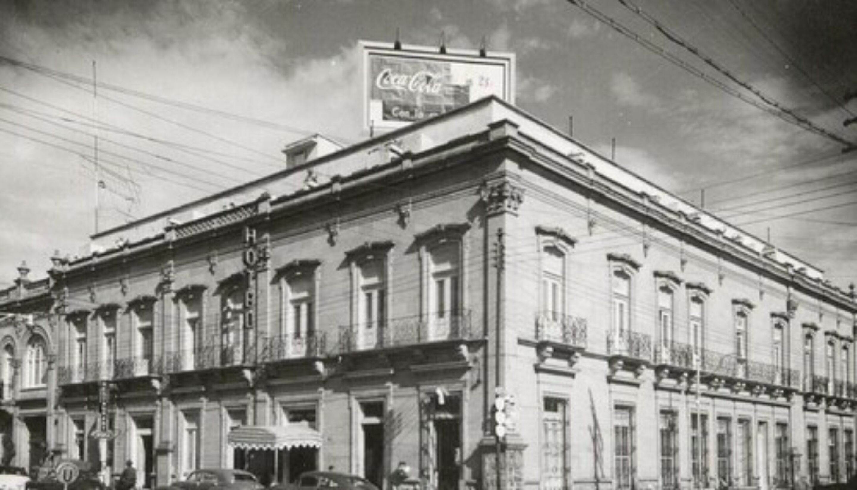 Un edificio histórico de arquitectura clásica, con un llamativo letrero de Coca-Cola en el tejado.