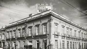 Un edificio histórico de arquitectura clásica, con un llamativo letrero de Coca-Cola en el tejado.