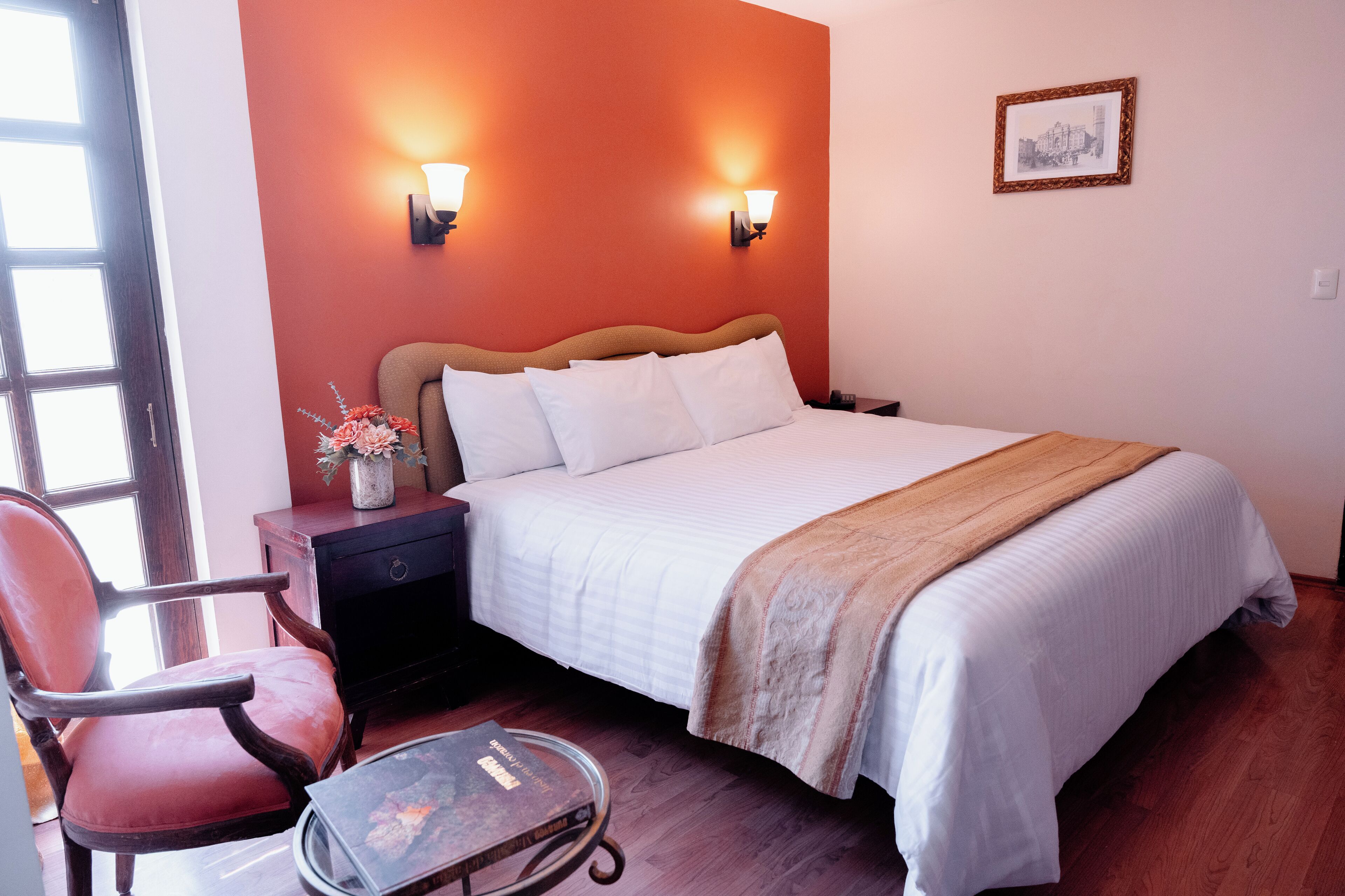 Ein Hotelzimmer mit Bett, Nachttisch, Stuhl und einem kleinen Tisch mit einem Buch.