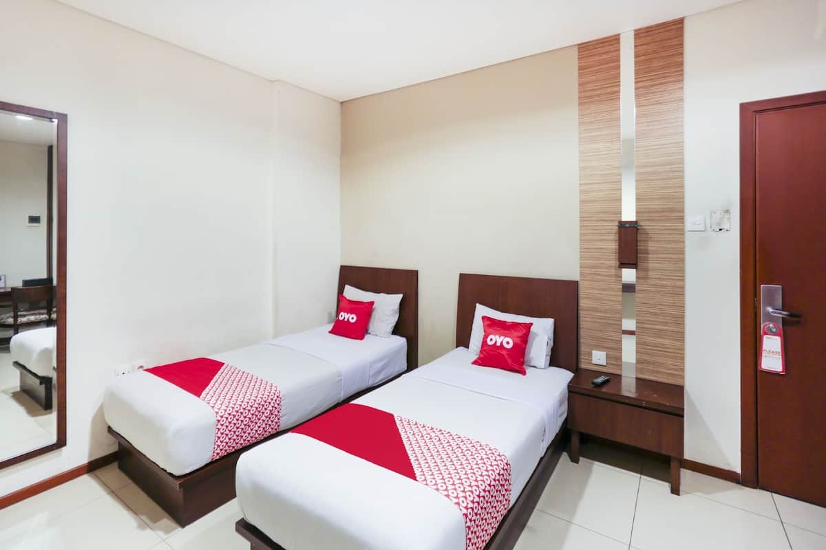 A hotel room with two single beds, each with a red and white patterned bedspread and a pillow labeled "OYO".