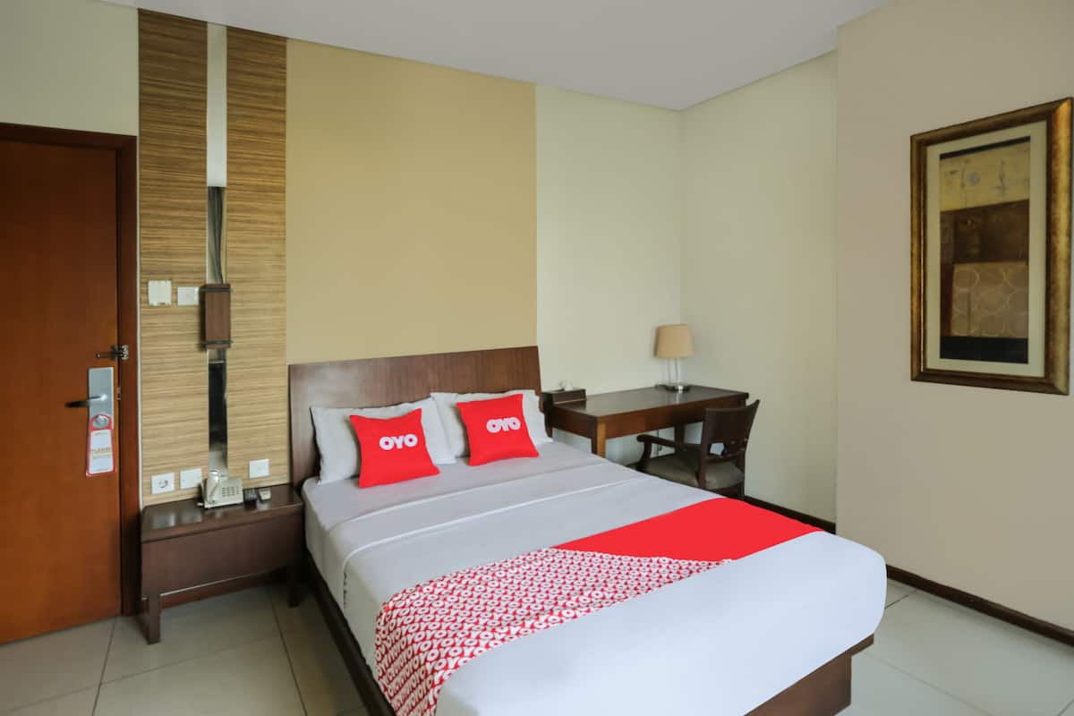 A hotel room with a bed, a desk, a chair, a lamp, and a painting on the wall.