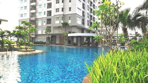 Una piscina con agua azul cristalina, rodeada de exuberante vegetación y un edificio moderno al fondo.