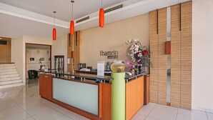 Un área de recepción con un mostrador de madera, un letrero que dice "thamin condo hotel" y una escalera al fondo.