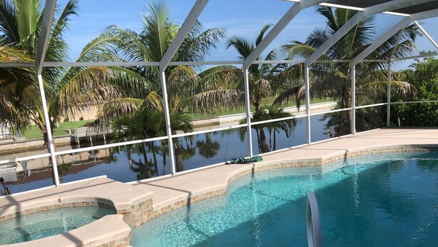 A pool with clear water, surrounded by palm trees and a covered area with chairs.