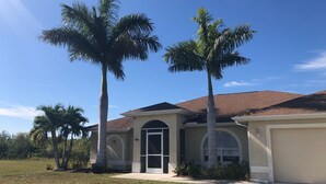 A single-story house with a brown tiled roof, a front door, and two palm trees in the front yard.