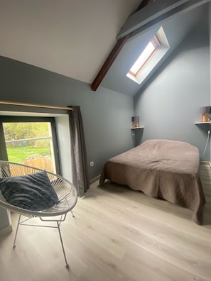 Un dormitorio con tragaluz, cama, sillón y vistas al exterior.