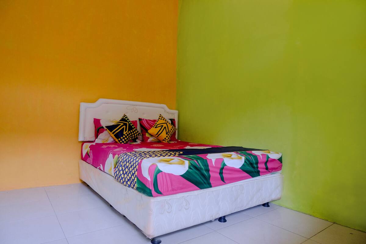Un lit avec une couvre-lit colorée et des coussins à motifs, le tout placé devant un mur jaune et vert.