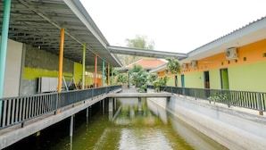 A canal with a pedestrian bridge, buildings with green and orange walls, and a metal roof structure.