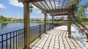 A wooden deck with a railing overlooking a body of water, with a pergola structure and potted plants. - Taragon by VillaDirect (Kissimmee)