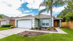 A single-story house with a garage, a well-maintained lawn, and a palm tree. - Taragon by VillaDirect (Kissimmee)