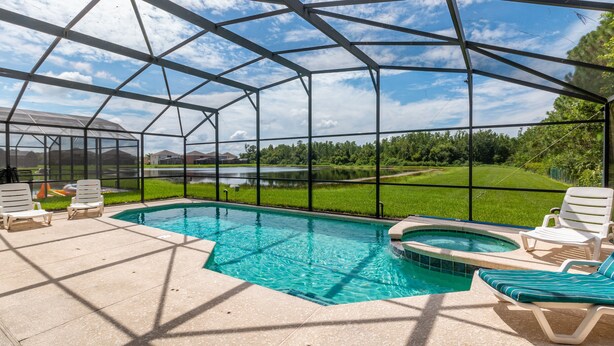 A covered outdoor swimming pool with lounge chairs and a view of a green landscape. - Taragon by VillaDirect (Kissimmee)