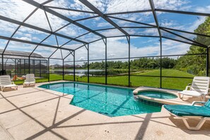 A covered outdoor swimming pool with lounge chairs and a view of a green landscape. - Taragon by VillaDirect (Kissimmee)