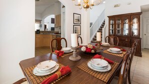 A dining room with a wooden table set for four, a chandelier, and a staircase leading to another level. - Sweet Retreat by VillaDirect (Kissimmee)