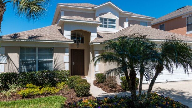 A two-story house with a front entrance, a covered porch, and a landscaped garden with various plants and flowers. - Sweet Retreat by VillaDirect (Kissimmee)