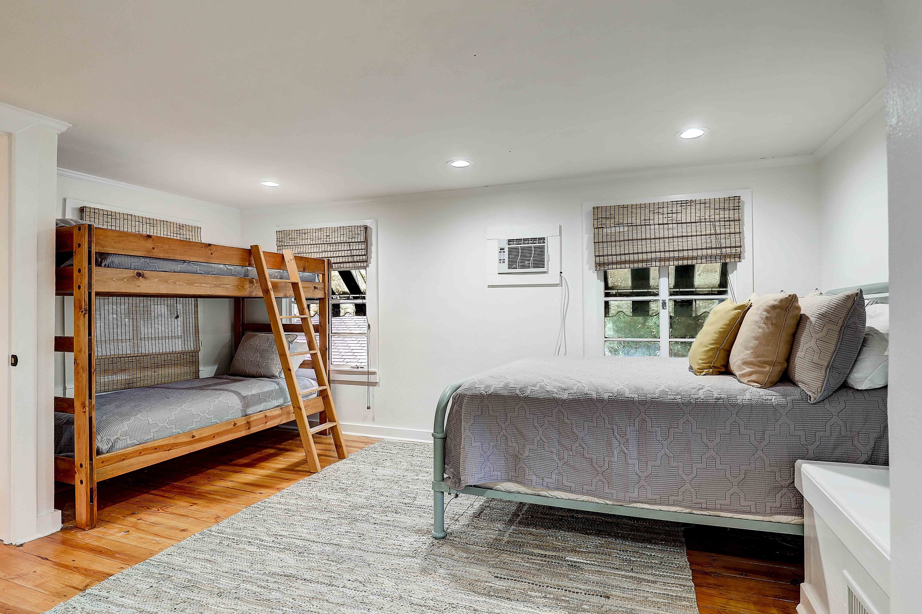 Un dormitorio con una cama litera, una cama individual, una escalera, un ventanal con persianas y un radiador.