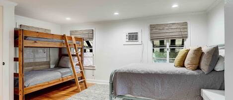 Un dormitorio con una cama litera, una cama individual, una escalera, un ventanal con persianas y un radiador.