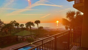 A pool area with a view of the sunset over the ocean, palm trees, and a gazebo. - Breathtaking sunsets and sunrises! (Indian Rocks Beach)